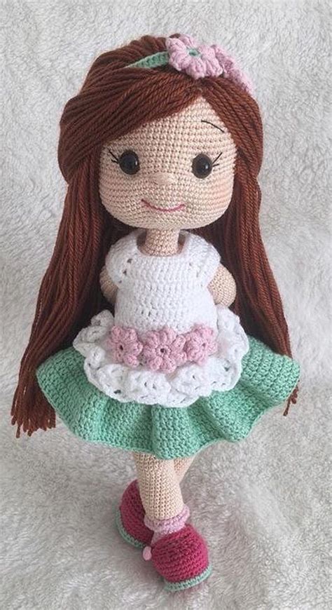 a crocheted doll with brown hair wearing a green dress and pink shoes on a white blanket