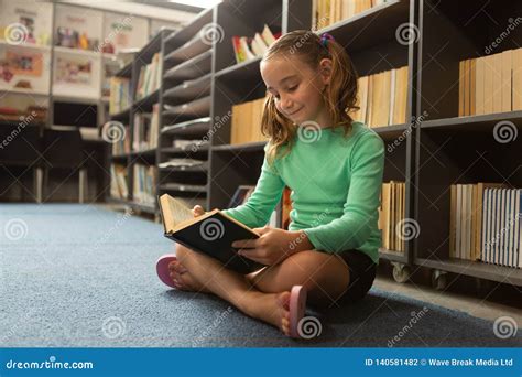 Schoolgirl Sitting On Floor In Cross Legged Position And Reading A Book