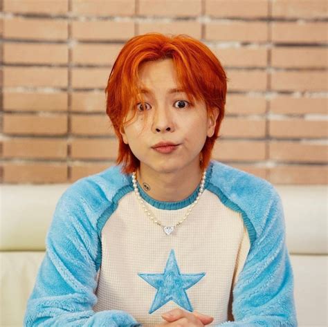 A Person With Red Hair And A Star On Their Shirt Is Sitting In Front Of A Brick Wall