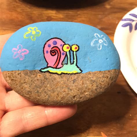 A Hand Holding A Painted Rock With A Snail On It