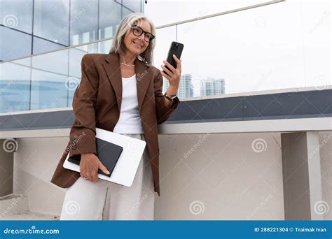 60 year old well groomed slender gray haired business woman dressed stylishly holds a smartphone