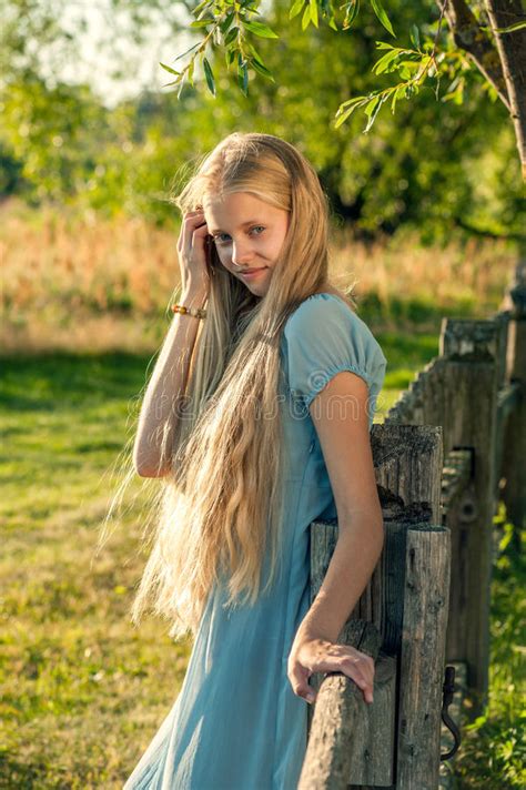 Blond Girl With Long Hair In Yellow Dress Sitting On A Bench Stock