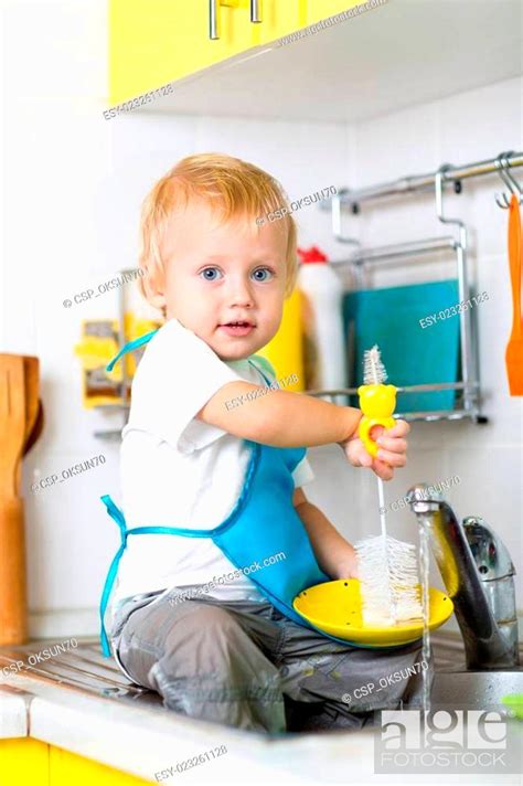 Child Boy Washing Dishes And Having Fun In The Kitchen Stock Photo