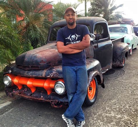 A Man Is Standing In Front Of An Old Truck With Orange Rims And His