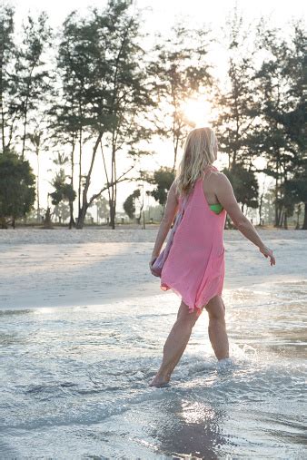 Woman Walk Along Beach In Sea Shallows At Sunrise Stock Photo