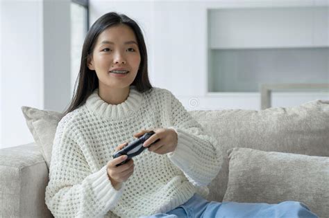 An Asian Woman Is Sitting On The Couch Holding A Joystick And Playing
