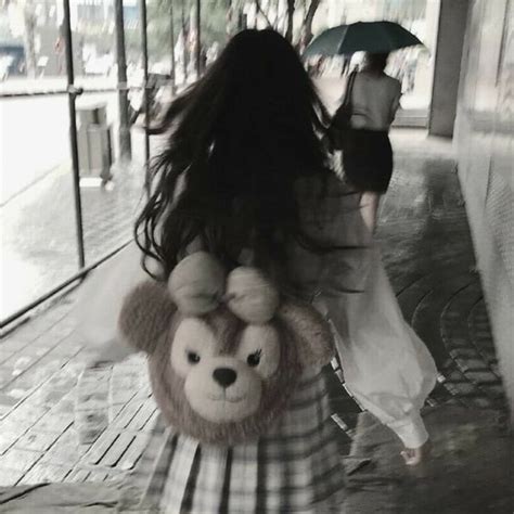 A Woman Walking Down A Street Holding An Umbrella And A Stuffed Animal