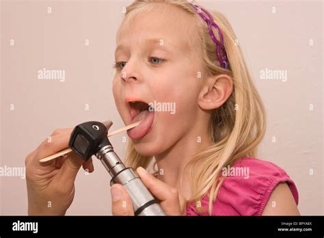 Young Girl Opens Her Mouth While Doctor Looks Inside Using A Tongue Depressor And Otoscope Stock