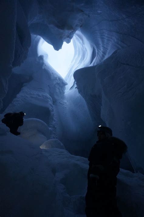 Two People Standing In An Ice Cave Looking At The Light Coming From