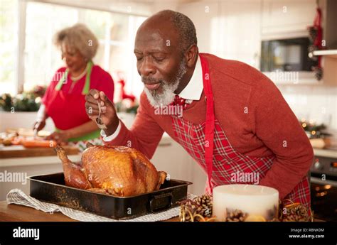 Senior Black Man Basting Roast Turkey In Preparation For Christmas Dinner His Wife Chopping