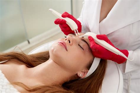 Beautiful Woman In Spa Clinic Receiving Stimulating Electric Facial Treatment From Therapist