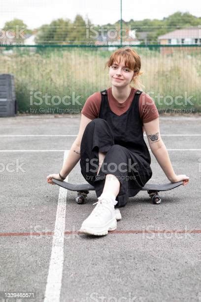 Female Student Sitting On A Skateboard In A Disused Tennis Court In A