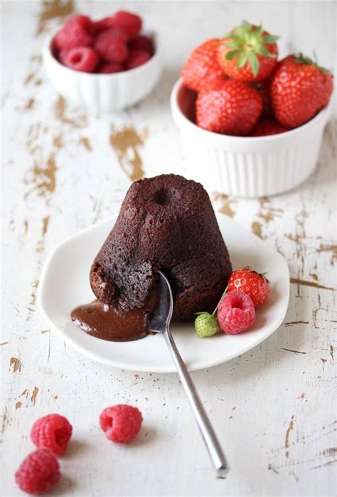 A Chocolate Cake On A White Plate With Raspberries In The Background And A Bowl Of Strawberries
