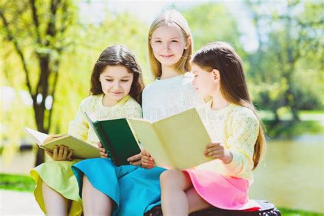 Libros De Lectura De Los Niños En El Parque Muchachas Que Se Sientan Contra árboles Y Lago Al