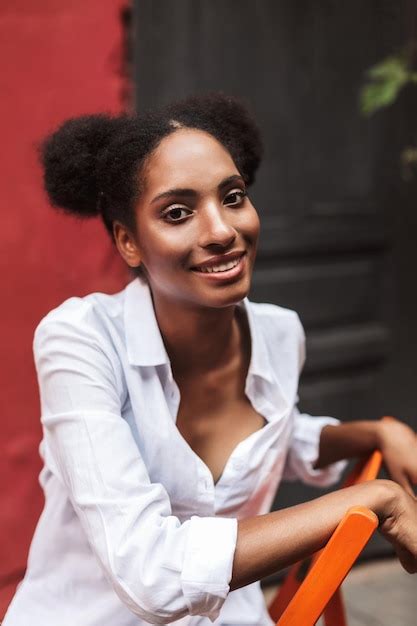 belle fille africaine souriante aux cheveux bouclés noirs en chemise blanche regardant