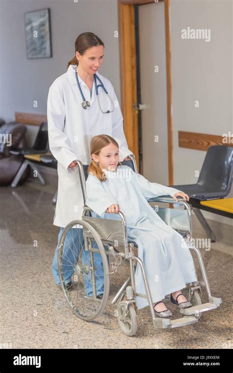 Doctor Wheeling A Patient In A Wheelchair In A Hospital Hallway Stock