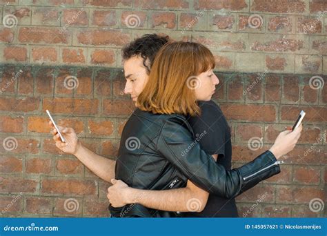 Young Couple Hugging While Each Staring At Their Own Smartphone Stock