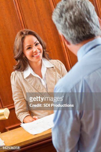 Friendly Hotel Manager Greeting Guest In Lobby At Checkin Desk High Res