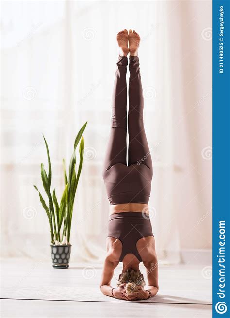 A Woman In Sportswear Practicing Yoga Performs An Inverted Asana In A