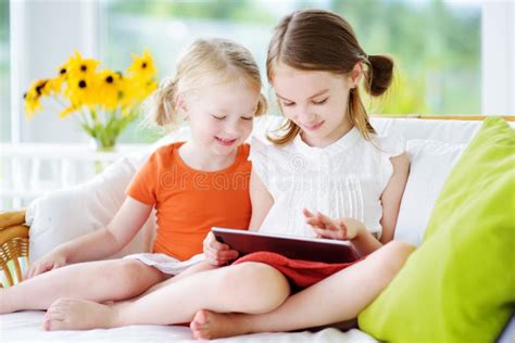 Two Adorable Little Sisters Playing With A Digital Tablet Stock Image