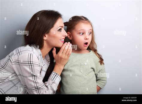 happy smiling mother whispering the secret to her surprising daughter in ear with on blue