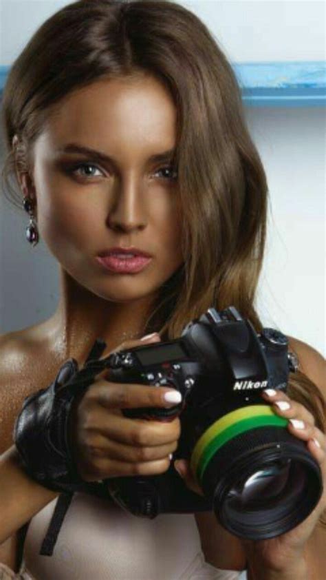 A Woman Holding A Camera In Her Right Hand And Looking At The Camera With An Intense Look On Her