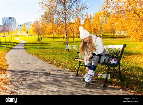 Blond Teen Girl With Long Hair In Autumn Park Sitting On The Bench And Putting On Roller Blades