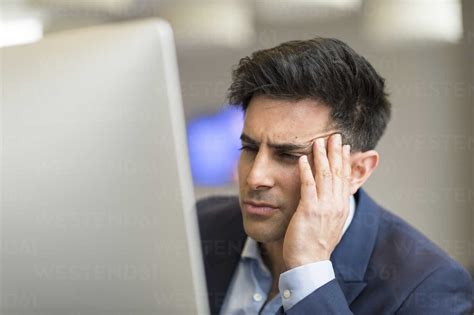 Confused Businessman Looking At Computer In Office Stock Photo