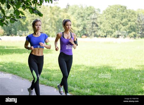two beautiful and attractive fitness girls are jogging in the park on a sunny morning stock