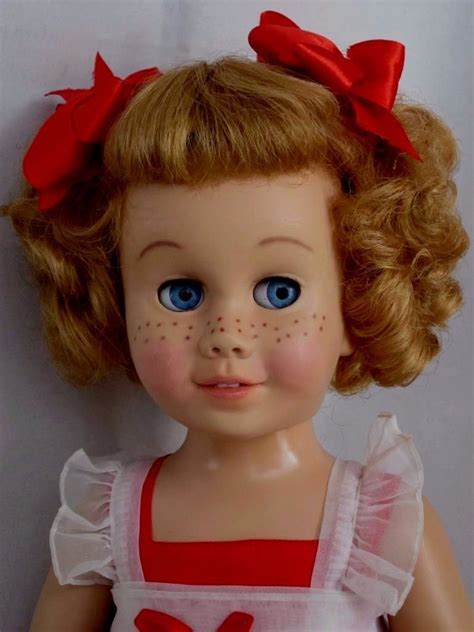 A Close Up Of A Doll With Blue Eyes And Blonde Hair Wearing A Red Dress