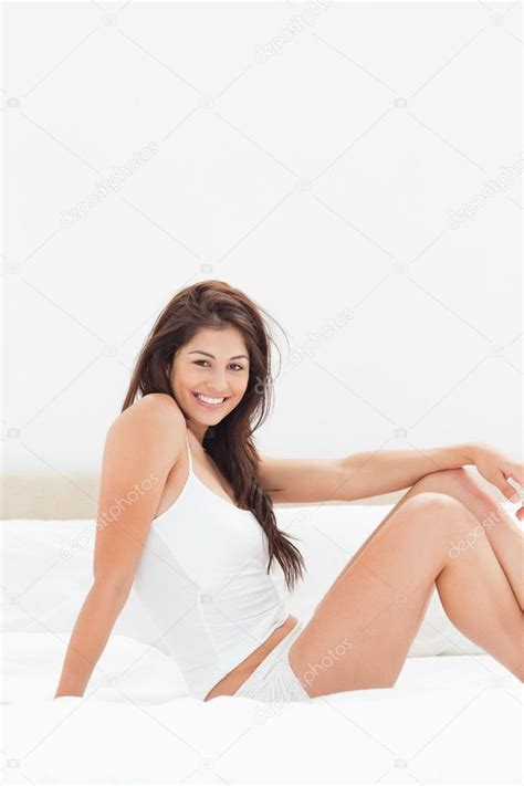 Woman Smiling And Sitting Sideways On The Bed With Both Knees U