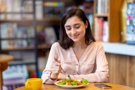 pretty latin lady tasting fresh healthy salad sitting at cafe or restaurant in daytime