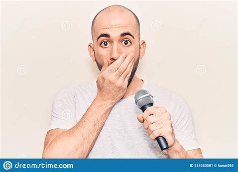 Young Handsome Bald Man Singing Song Using Microphone Covering Mouth With Hand Shocked And