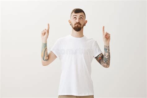 Handsome Stylish Caucasian Urban Guy With Beard And Tattoos Pointing And Looking Up With