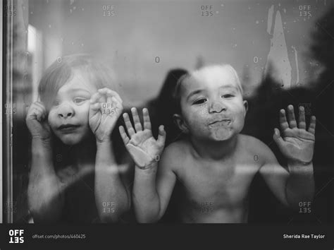 Two Young Children With Their Faces Pressed Against Glass Window Stock