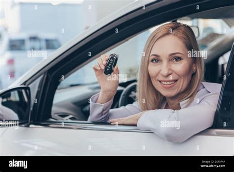 Happy Mature Woman Sitting In Her New Automobile Smiling Joyfully To The Camera Holding Car