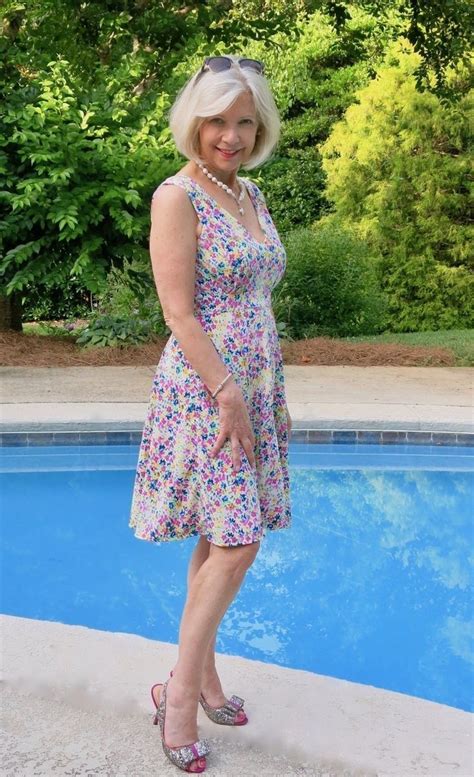 an older woman standing in front of a swimming pool wearing sandals and a floral dress