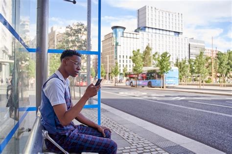 Premium Photo Man Waiting At Bus Stop While Looking At Smart Phone