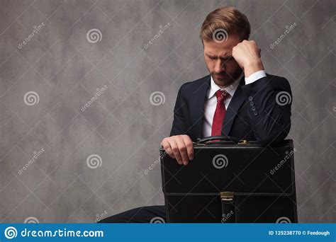 Sad Young Businessman Sitting And Holding His Briefcase Stock Photo