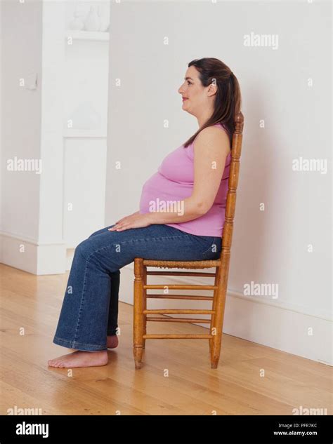 Pregnant Woman Sitting Upright In Chair Hands Resting On Her Knees Bare Feet Firmly On The