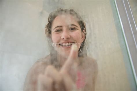 Portrait Of Young Woman In Shower Drawing On Steamed Glass Doorの写真素材