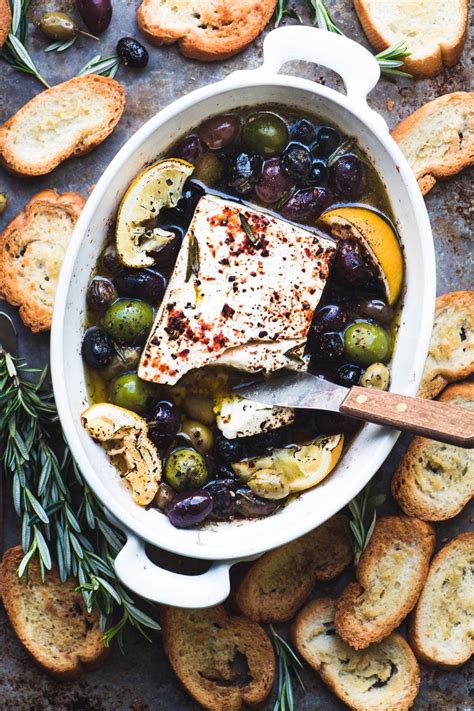 10 best dinner appetizers of march 2021. overhead shot of baked feta cheese with olives, lemon, and ...