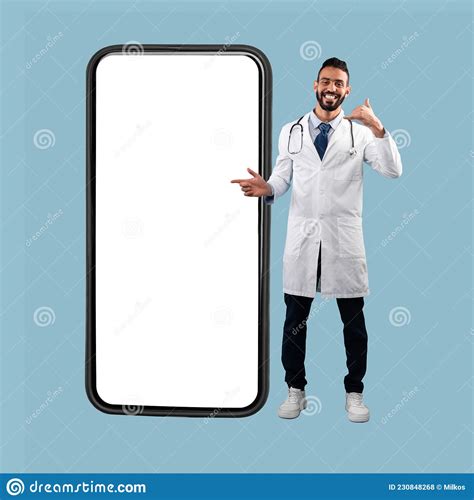 Arabic Doctor Pointing at Cellphone Gesturing Call Me, Blue Background ...