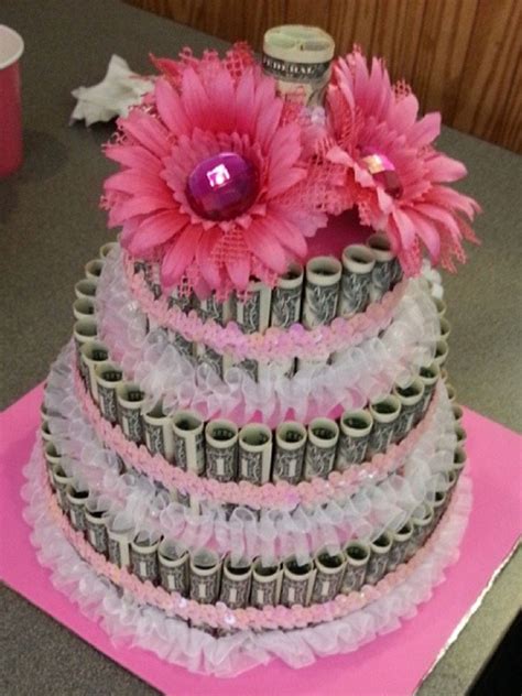 A Three Tiered Cake Decorated With Pink Flowers And Dollar Bills On The