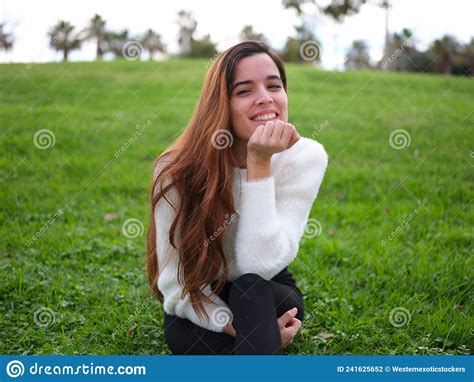A Young Woman In Love Sitting On The Grass In The Park Smiling At