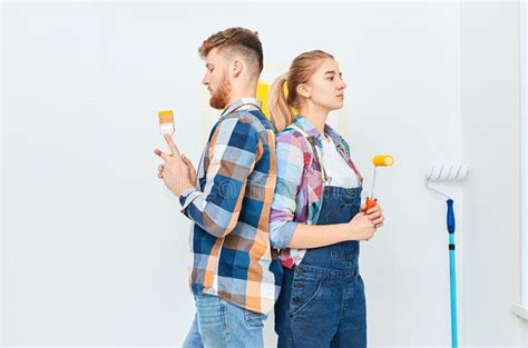 Smiling Couple Painting At Home Holding Paint Roller And Brush