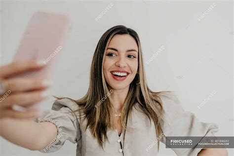 smiling woman taking selfie through mobile phone against white background — beautiful woman