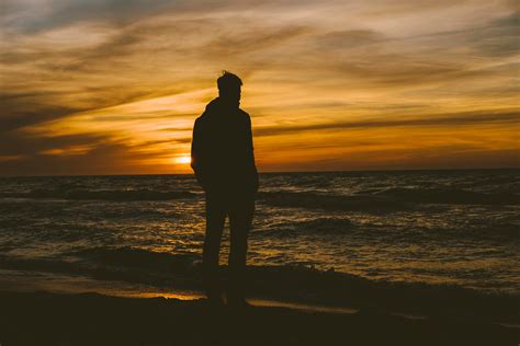 Silhouette Of Person Standing On Seashore During Sunset · Free Stock Photo