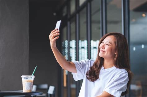 Una Hermosa Joven Asiática Usando Un Teléfono Móvil Para Tomarse Una Selfie En Un Café Foto