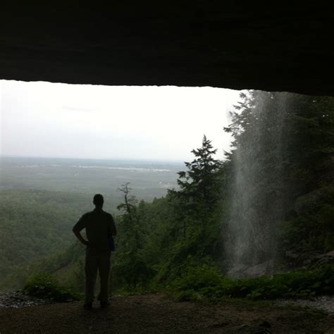 A Man Standing In Front Of A Waterfall Looking Out At The Valley And